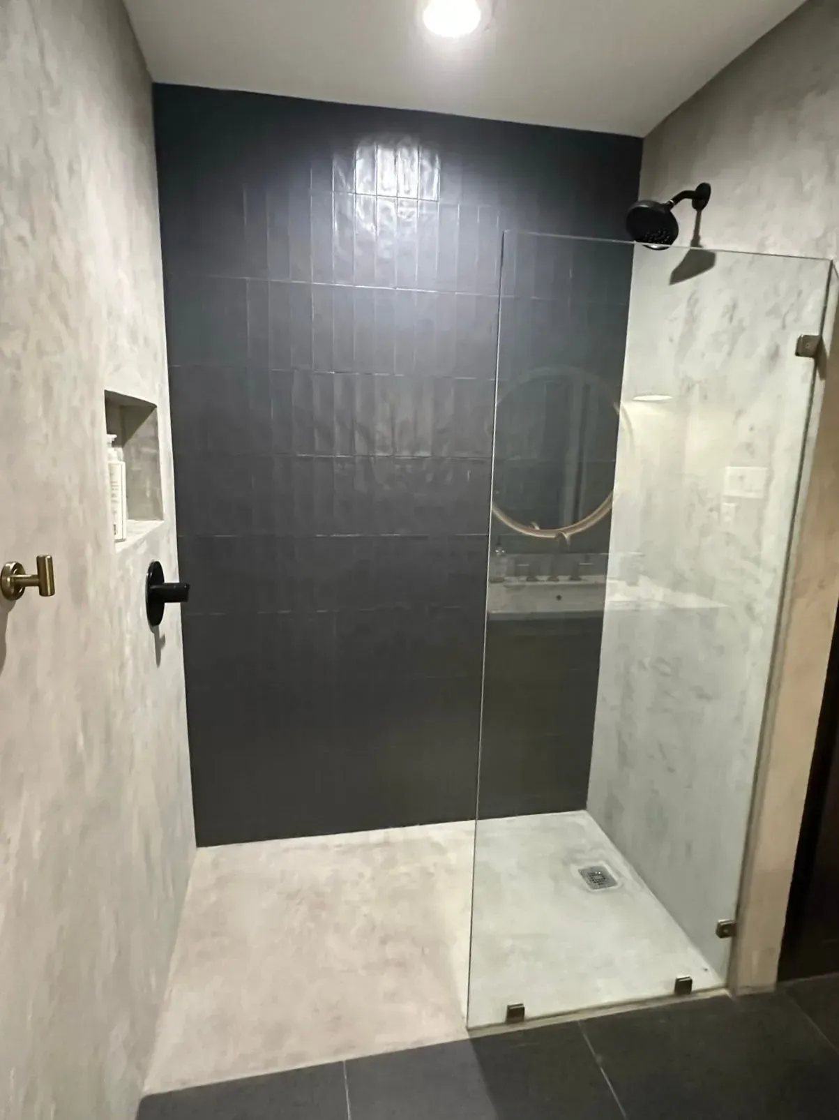 Modern shower with black tiled wall, glass door, and gray walls.