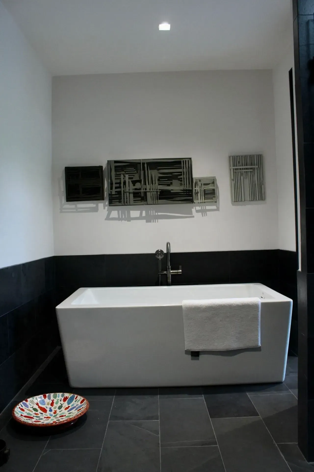 Bathroom with white tub, black tile, white walls, and artwork.