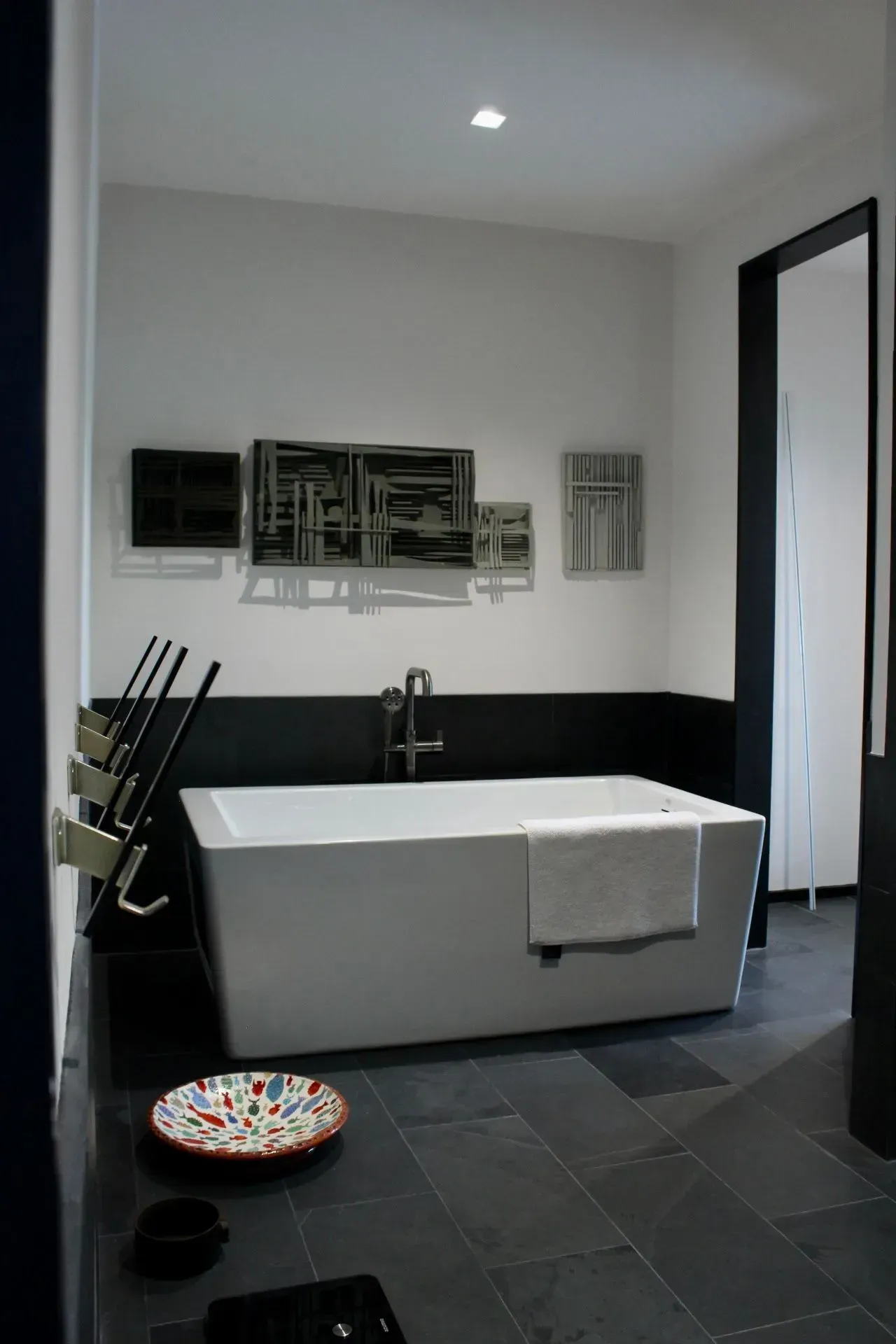 Modern bathroom with a white tub, dark walls, and art.