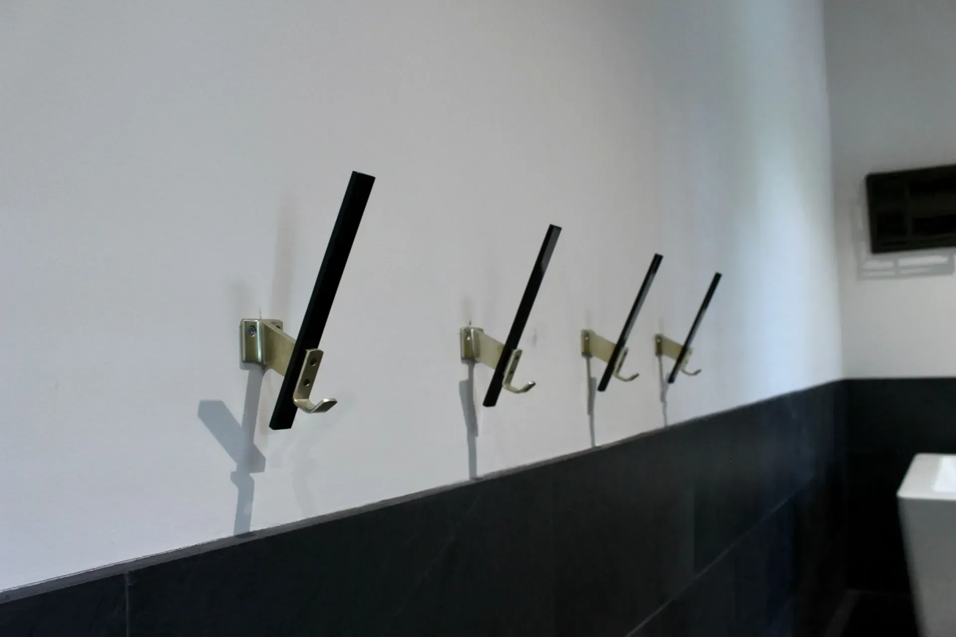 Black hooks on a white wall above a black tiled border.