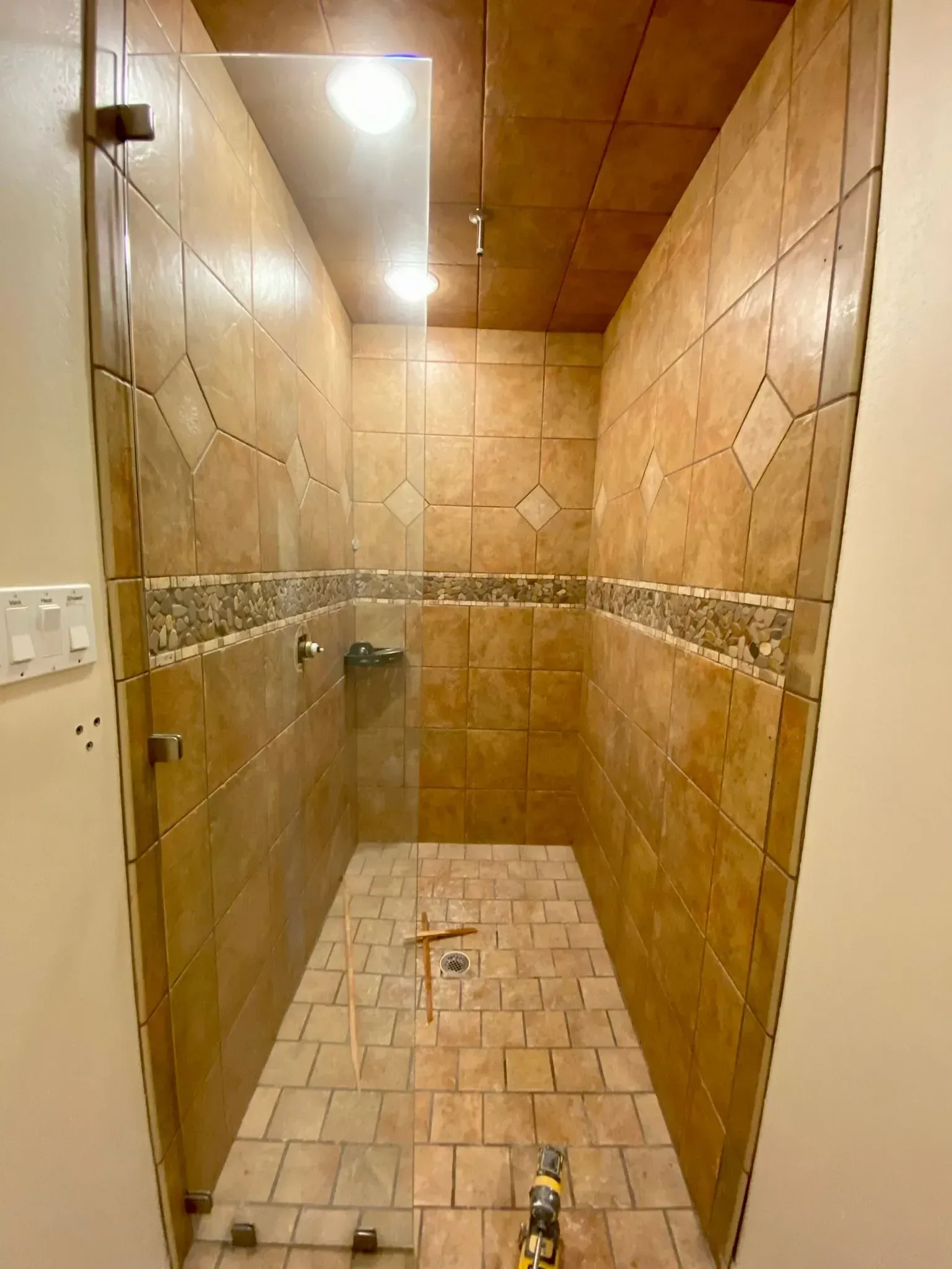 Walk-in shower with beige tile walls, glass door, and tiled floor, recessed lighting.