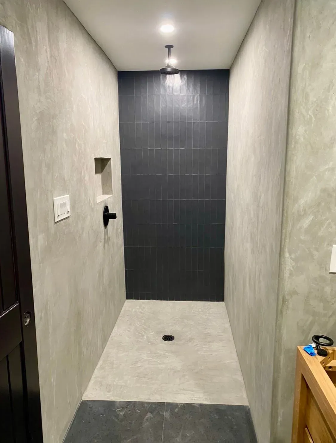 Gray-walled shower with black tile accent, recessed shelf, and dark fixtures.