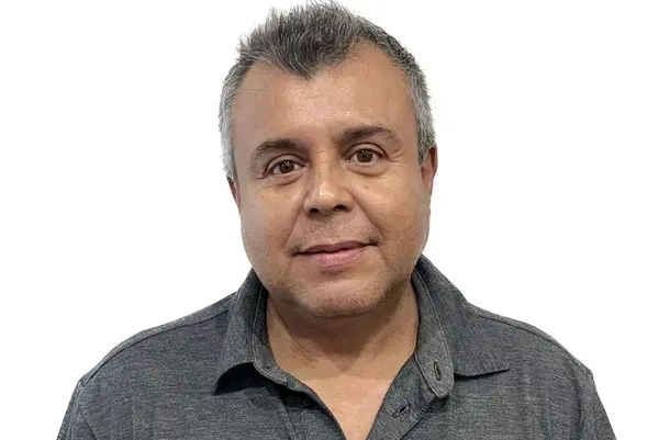 Man with graying hair in a gray shirt, smiling against a white background.