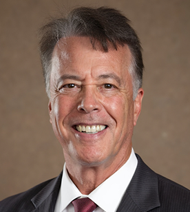Smiling man in a dark suit and white shirt against a neutral background