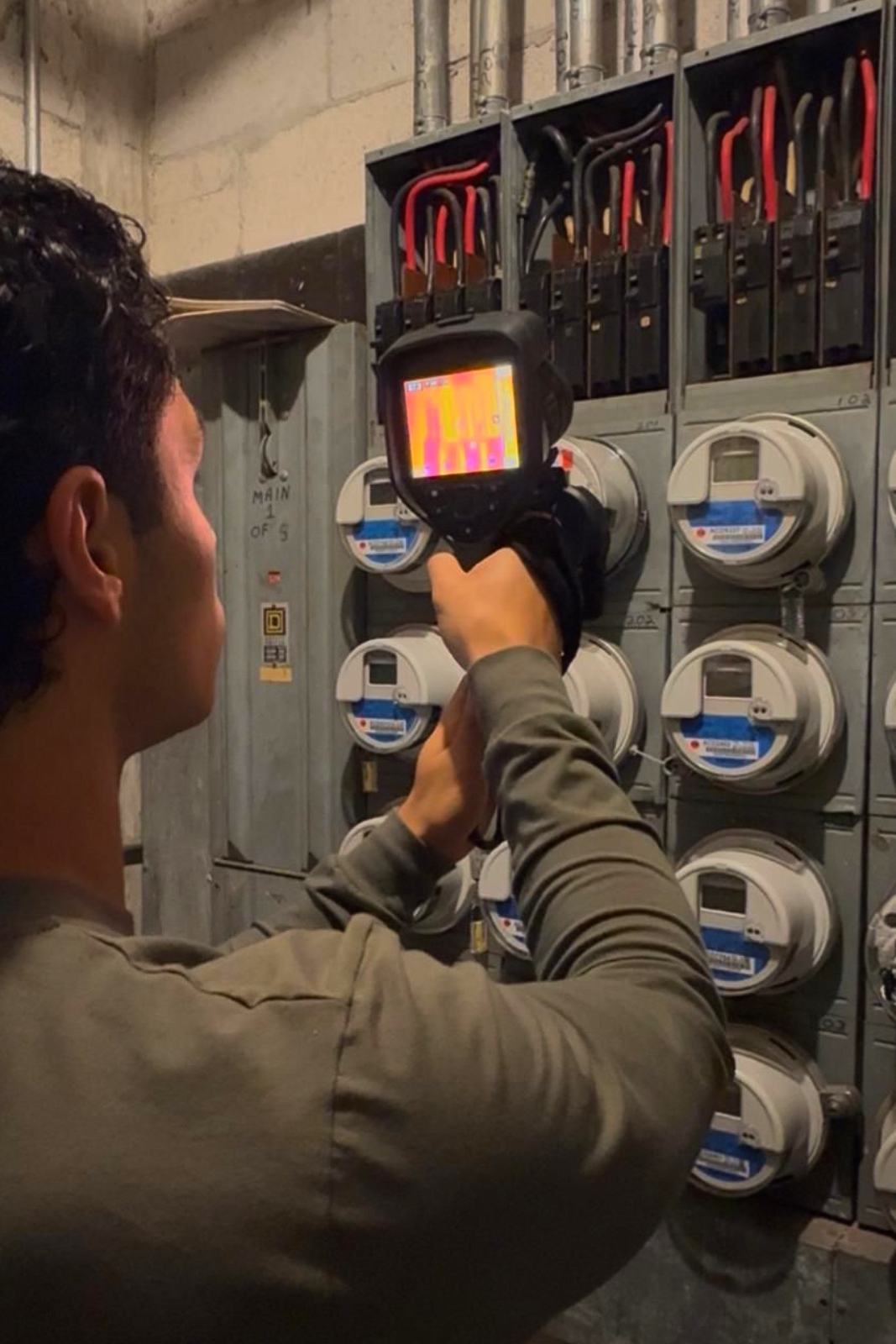 Technician using a thermal camera to inspect electrical meter panels in a utility room