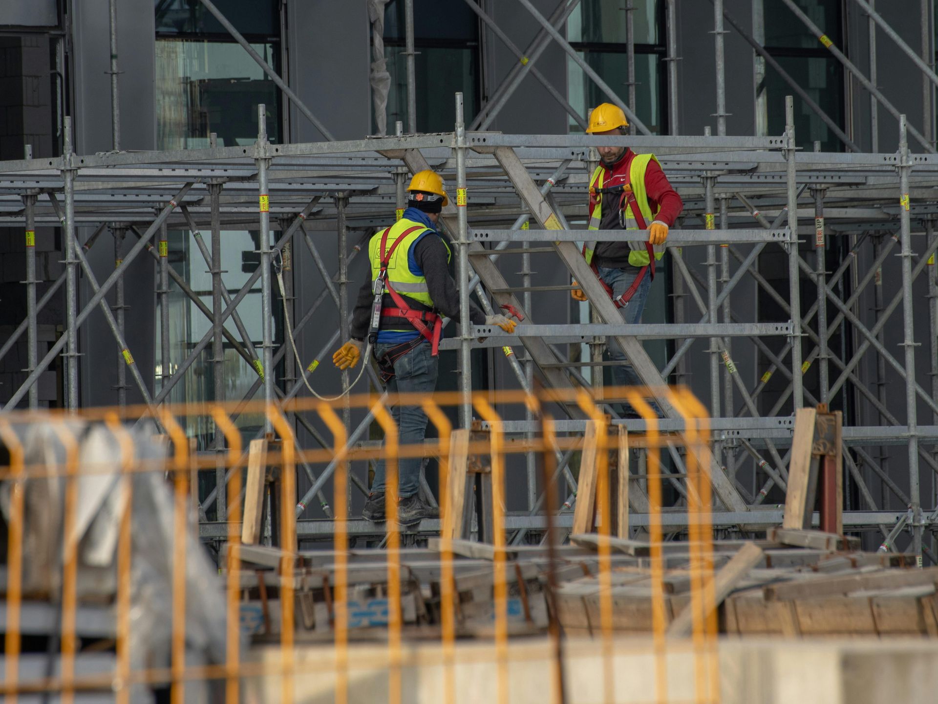 Construction workers in yellow hard hats and safety vests working on scaffolding at a building site