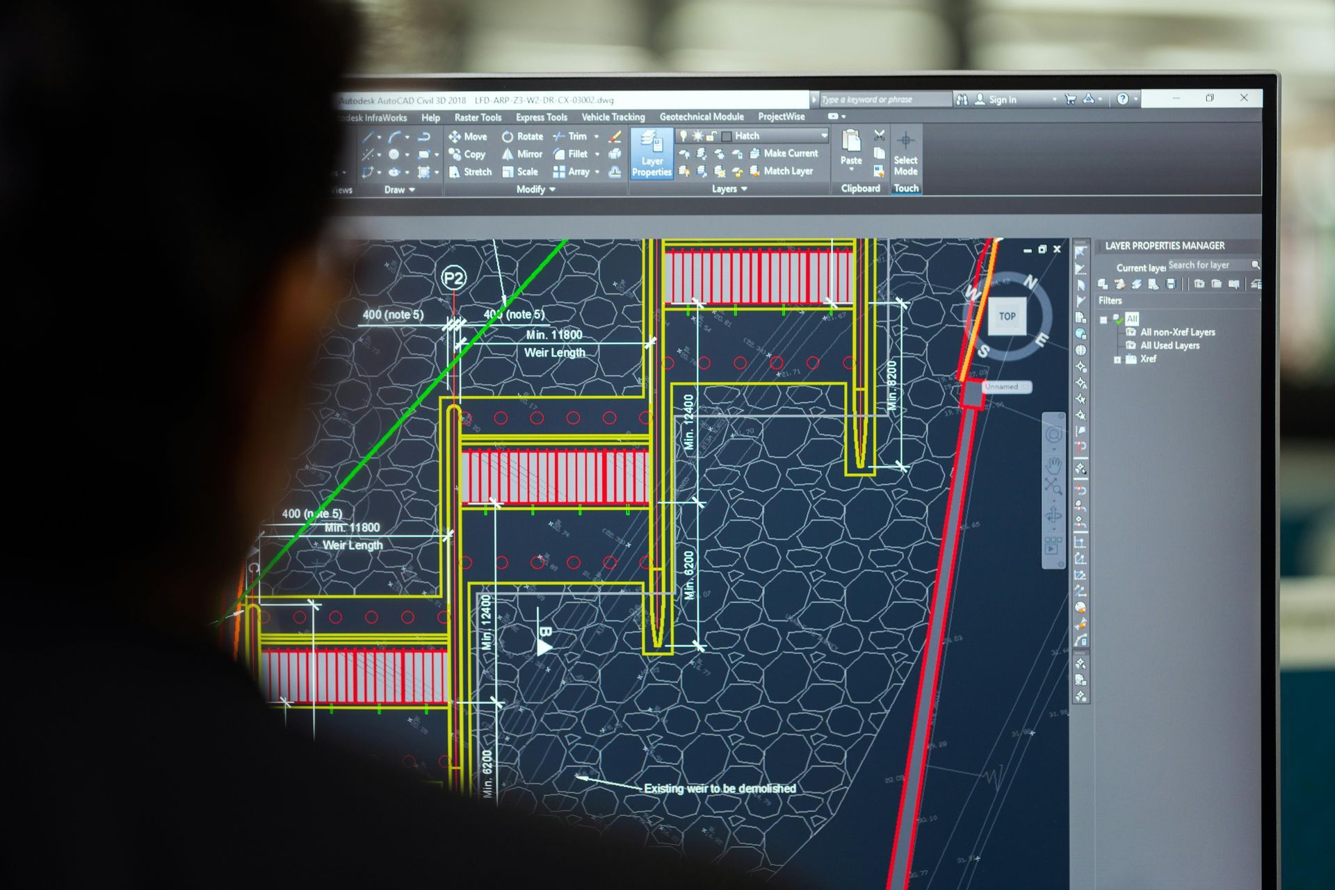 Person viewing a CAD floor plan on a computer monitor with dark interface and colorful lines