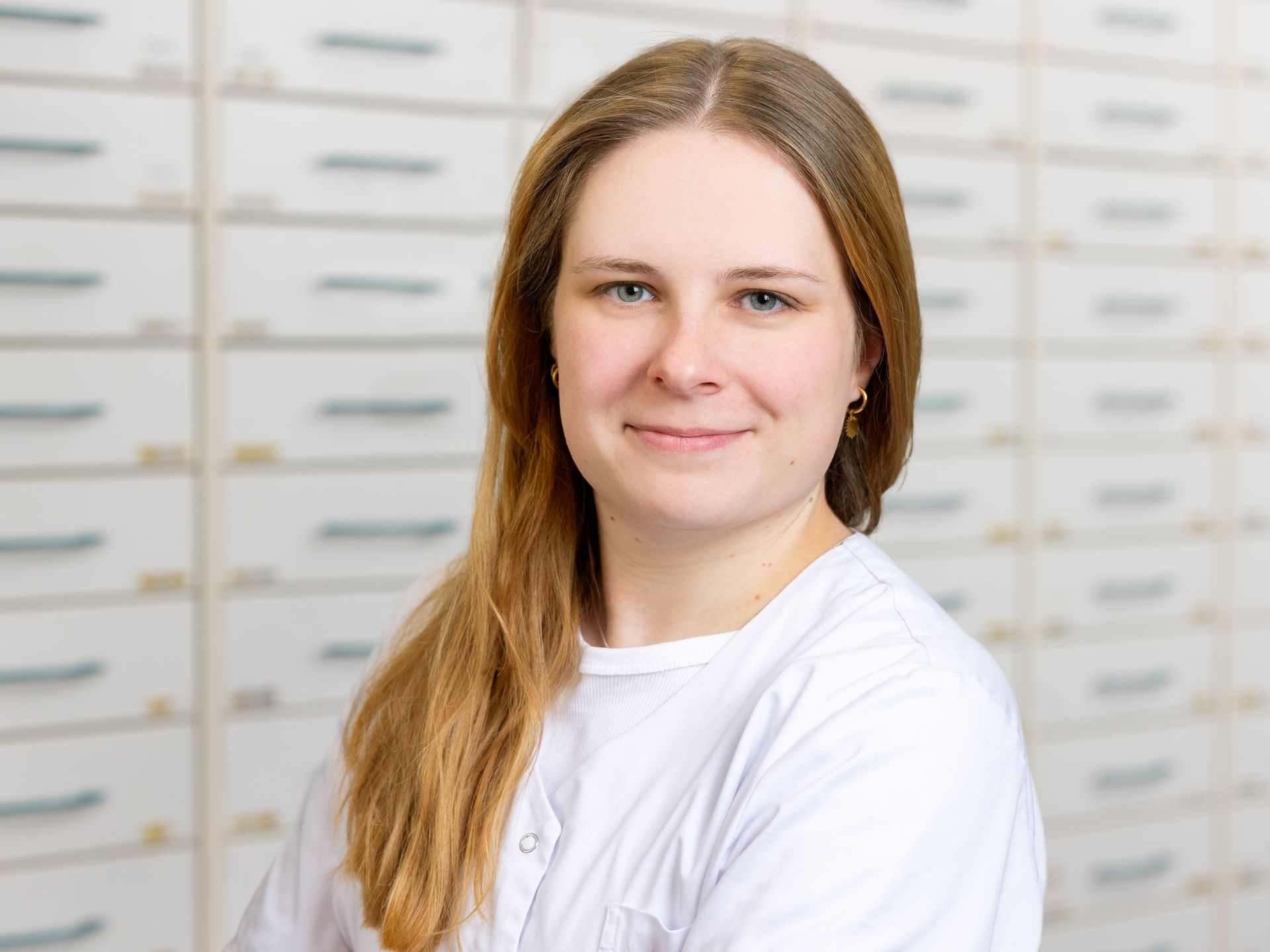 Eine Frau in einem weißen Laborkittel steht vor einer Schubladenwand.