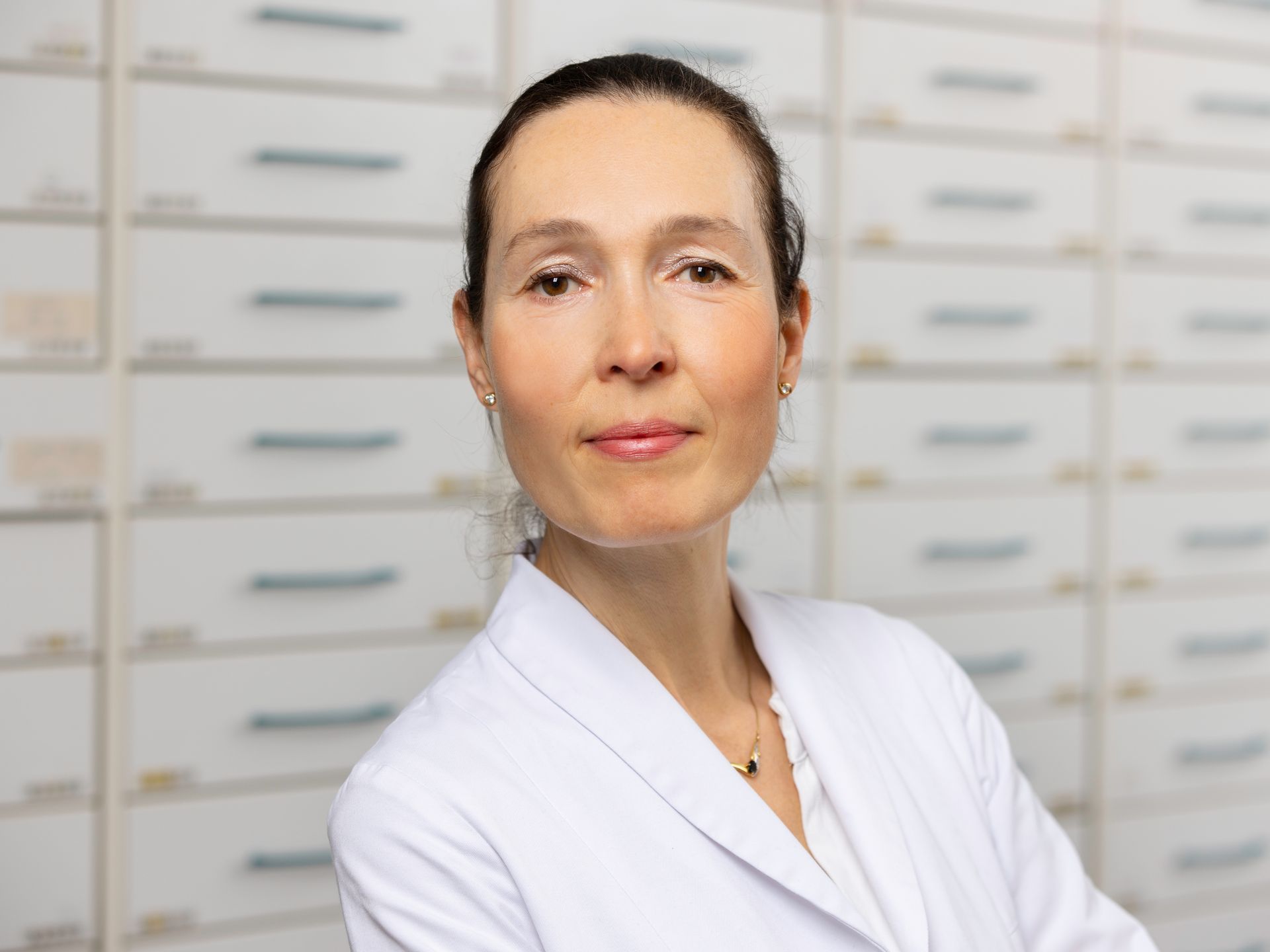 Eine Frau im weißen Kittel steht in einer Apotheke vor einer Reihe von Schubladen.