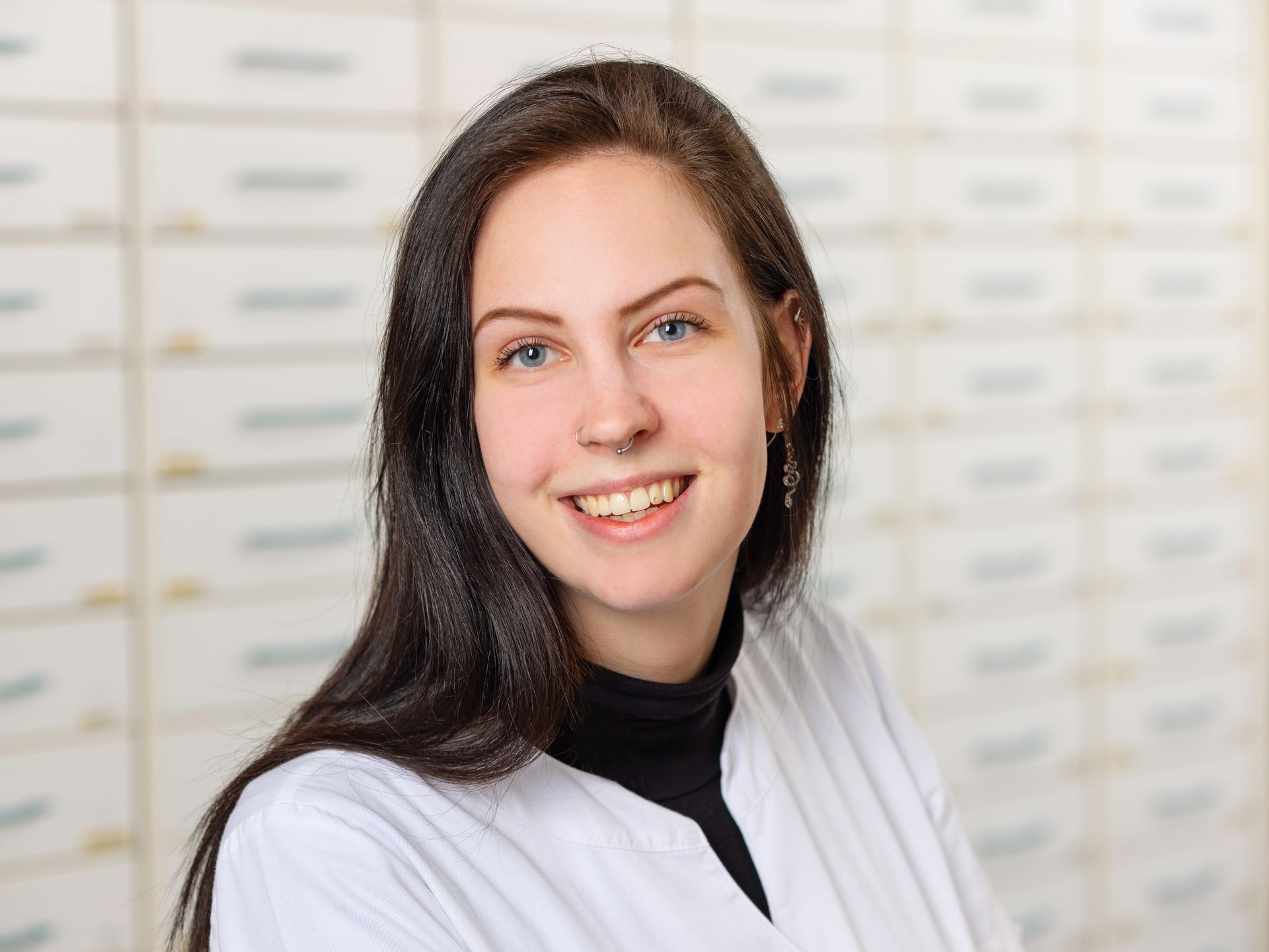 Eine Frau im weißen Kittel lächelt vor einer Apotheke.