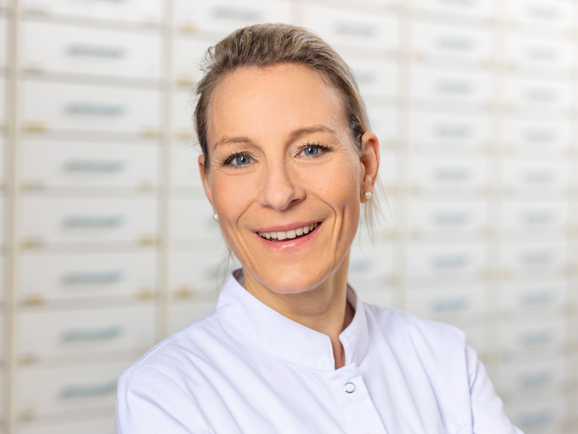 Eine Frau in einem weißen Laborkittel lächelt und hat die Arme vor der Brust verschränkt.