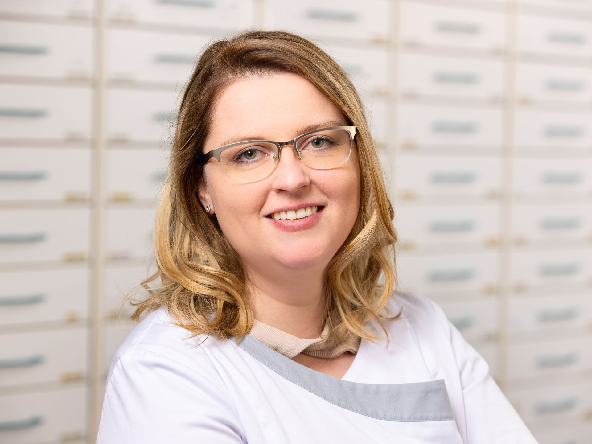 Eine Frau mit Brille und weißem Kittel lächelt in die Kamera.