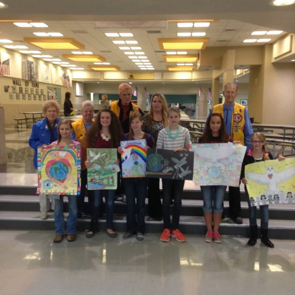 A group of people are posing for a picture while holding paintings