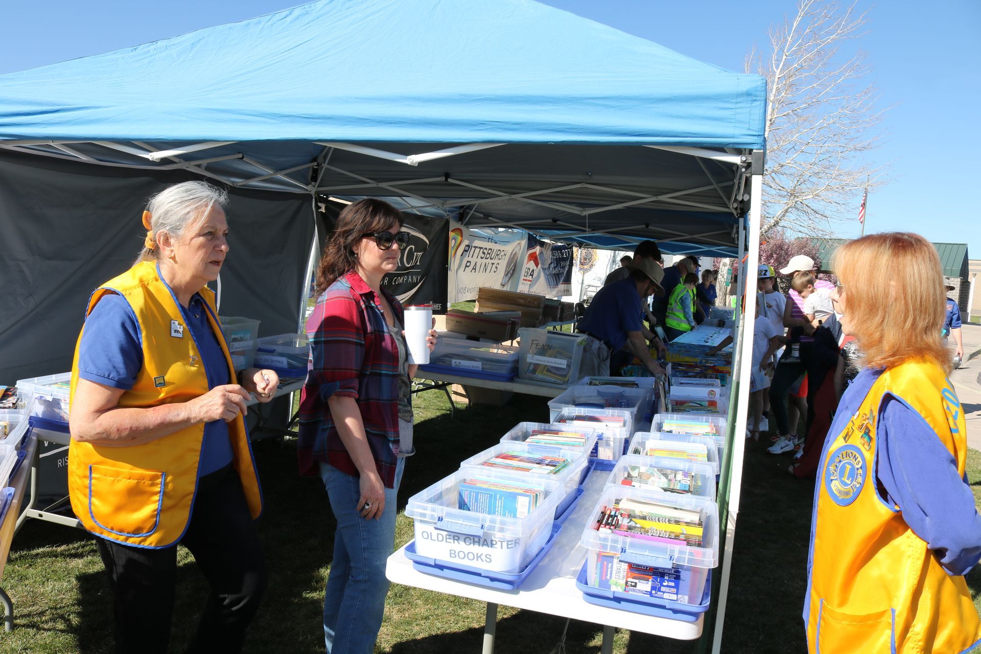 Two women in yellow vests are standing in front of a table with boxes on it.