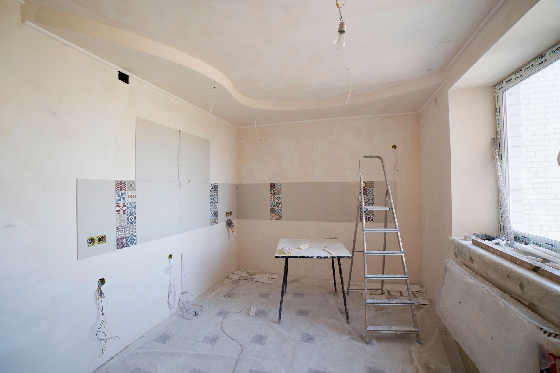 Partially renovated room with white walls, ladder, worktable, and construction dust