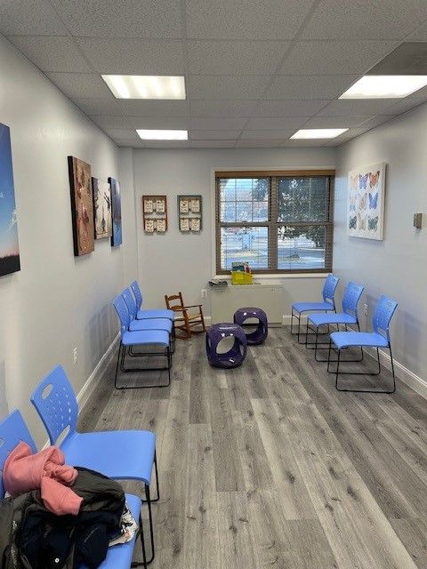A waiting room with blue chairs and purple ottomans