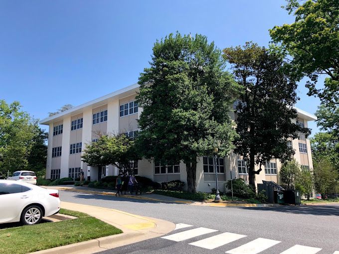 A white car is parked in front of a large white building