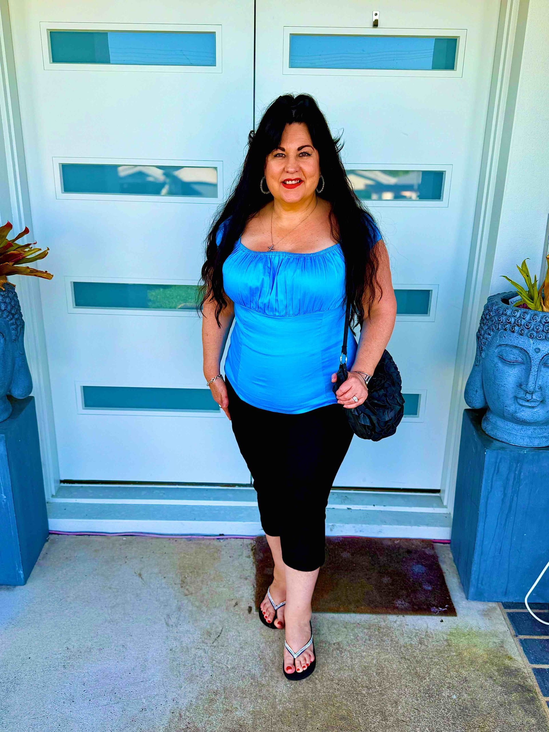 Vivian Mizzi in blue top and black capri pants stands in front of white doors.