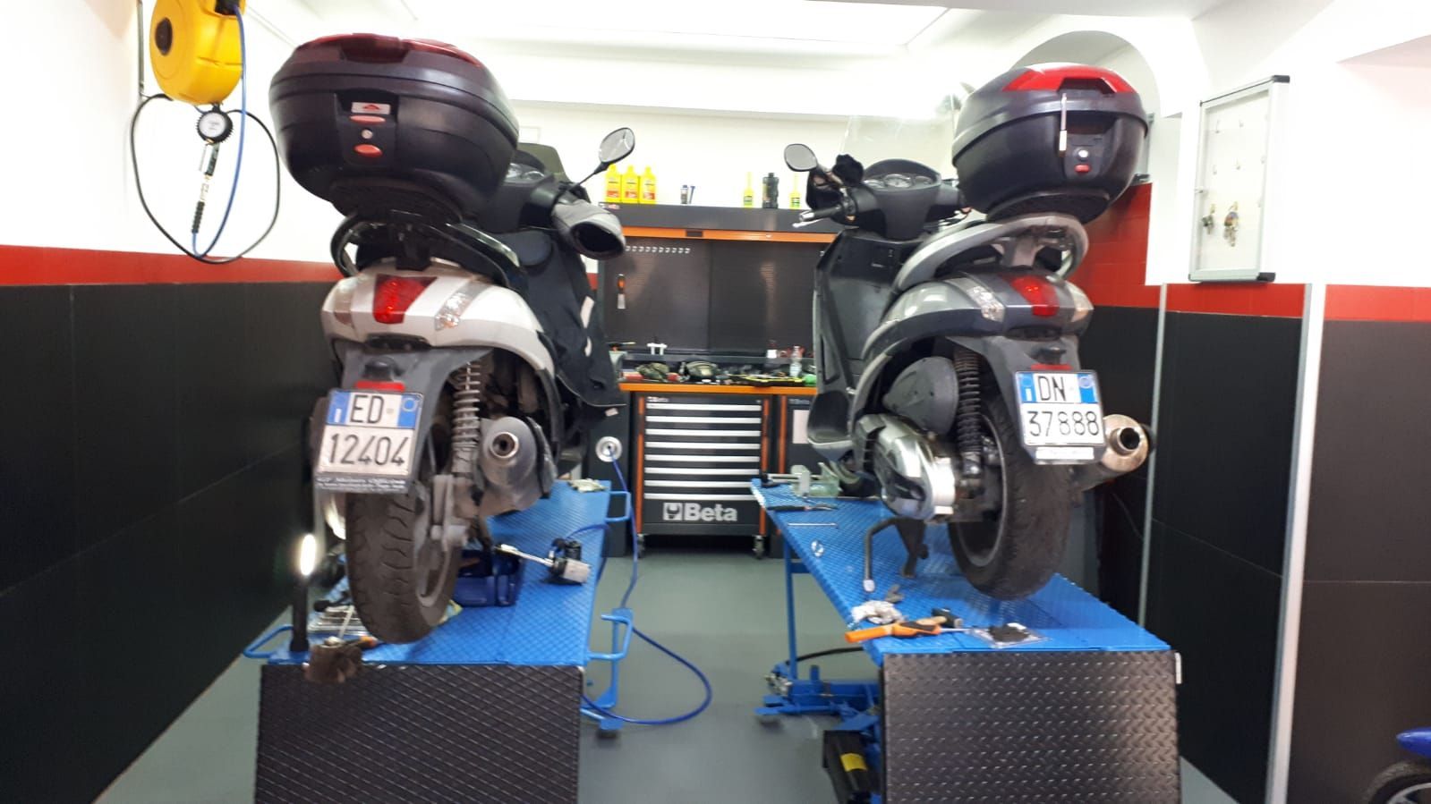 Two motorcycles are sitting on a lift in a garage.