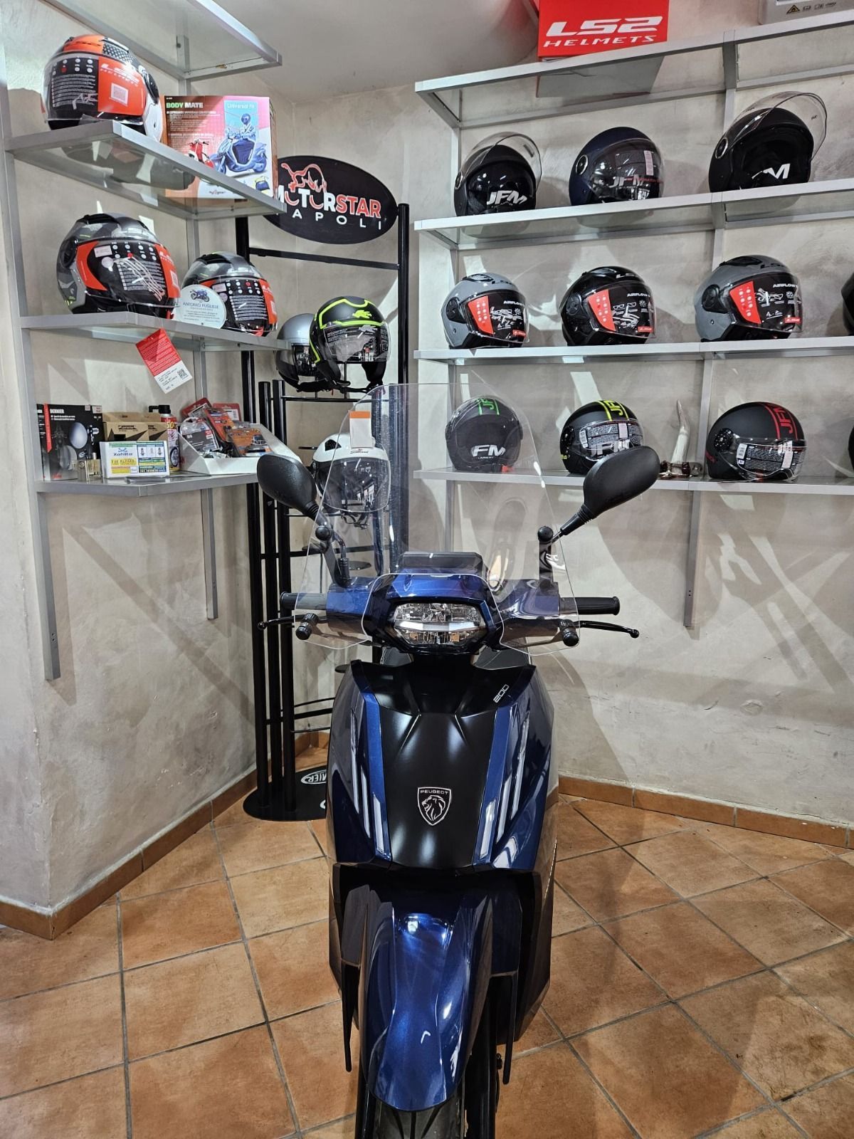 A blue motorcycle is parked in a room filled with helmets.