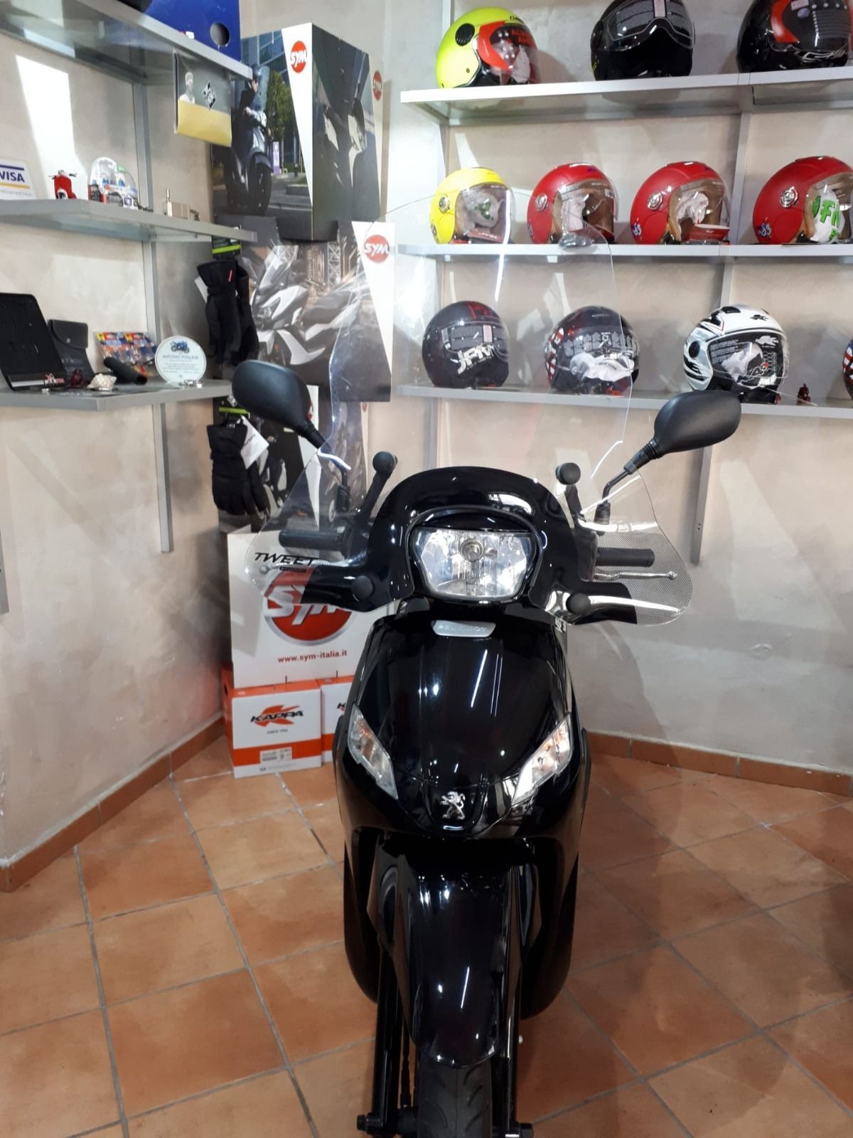 A black scooter is parked in a room with helmets on shelves.