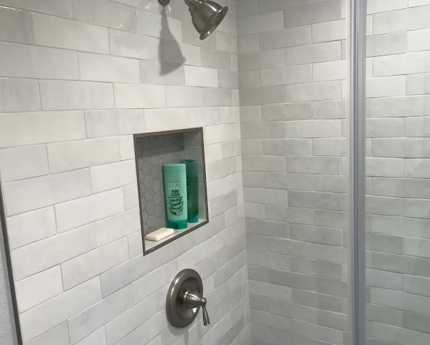 A shower with white tiles and a soap dispenser in a niche.