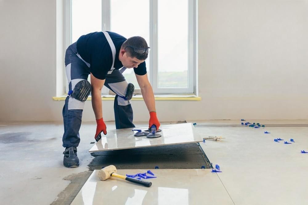 A man is laying a tile floor in a room.