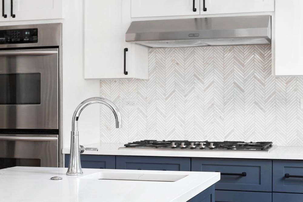 A kitchen with blue cabinets , white counter tops , stainless steel appliances and a stove top oven.