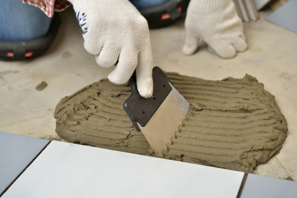 A person is applying adhesive to a tile with a spatula.