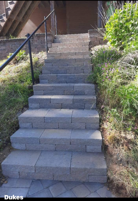 Stone steps leading upwards, with a black handrail on the left, set into a hillside.