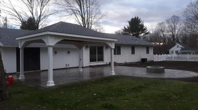 White house with a patio and attached covered seating area, circular fire pit in yard.