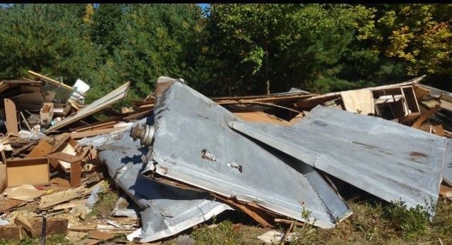 Debris pile of wood and metal against a backdrop of trees, likely from a demolition.