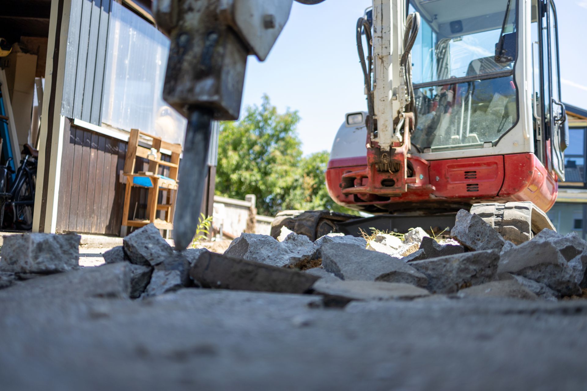Mini excavator with hydraulic hammer breaking concrete.