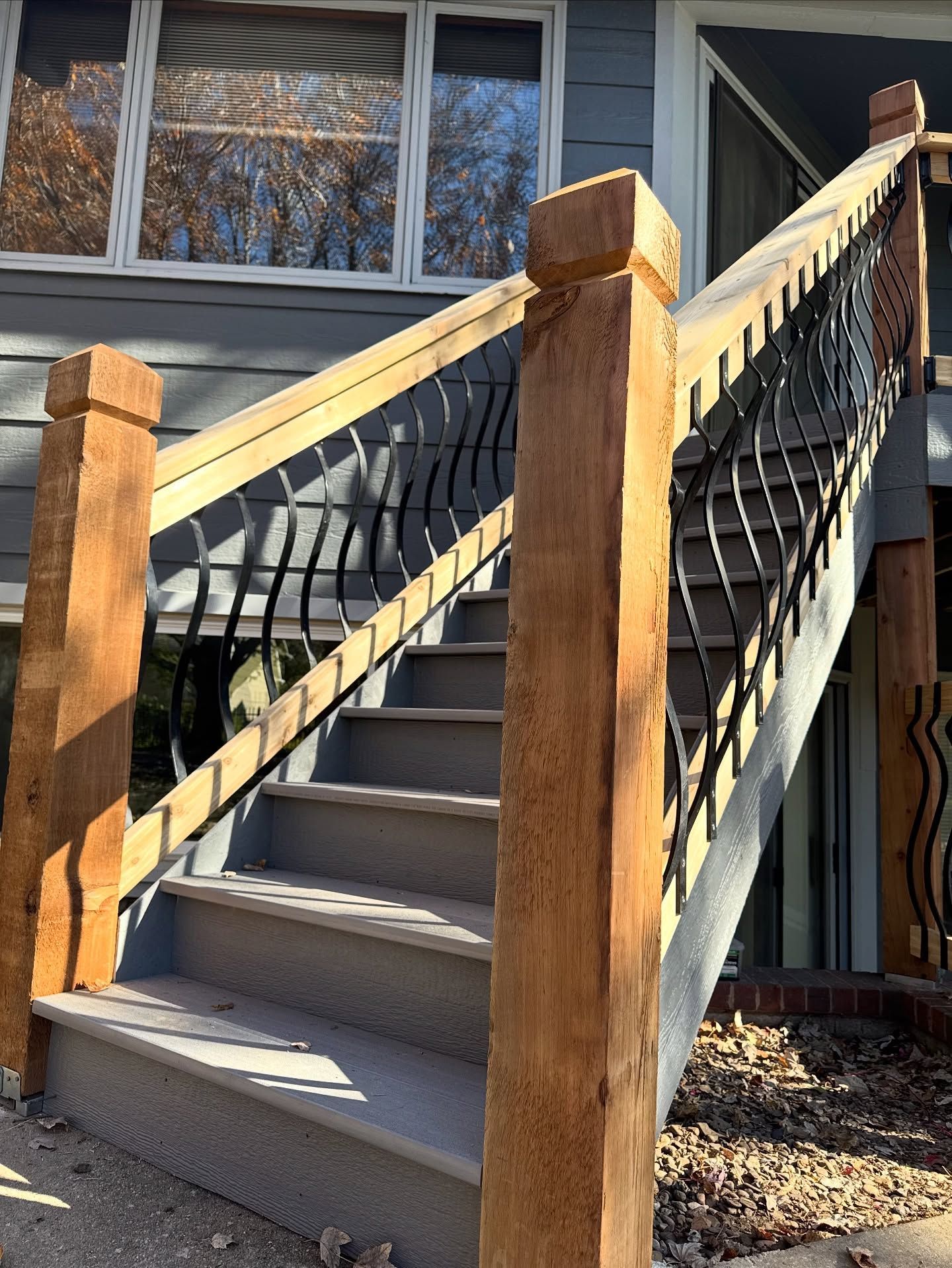 Outdoor staircase with gray steps, thick wooden posts, and black curved metal railings leading up to a house entrance.