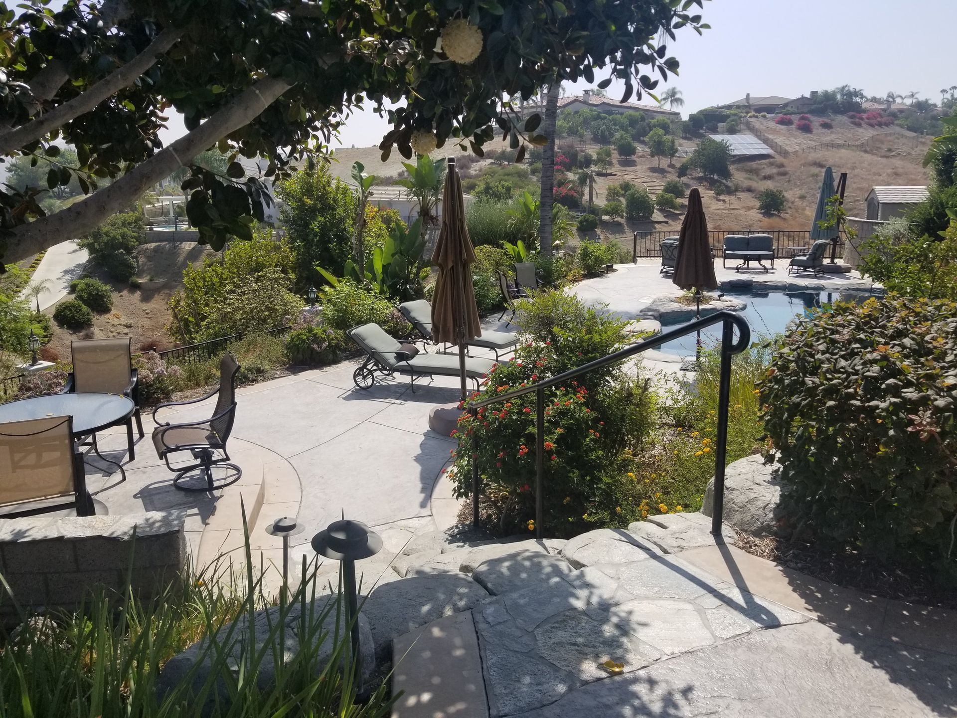 A patio with chairs and umbrellas and a staircase leading to a pool