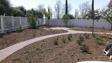 A brick walkway leading to a house with a white fence.