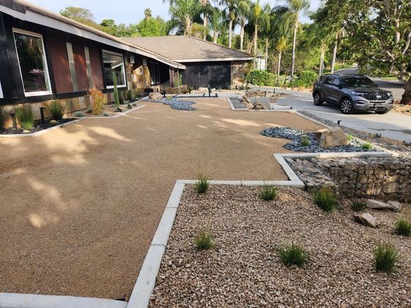 A car is parked in front of a house with a gravel driveway.