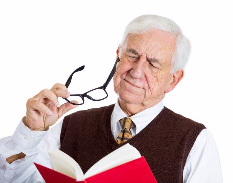 photo of an older gentleman holding a book and a pair of glasses with a disgruntled appearance