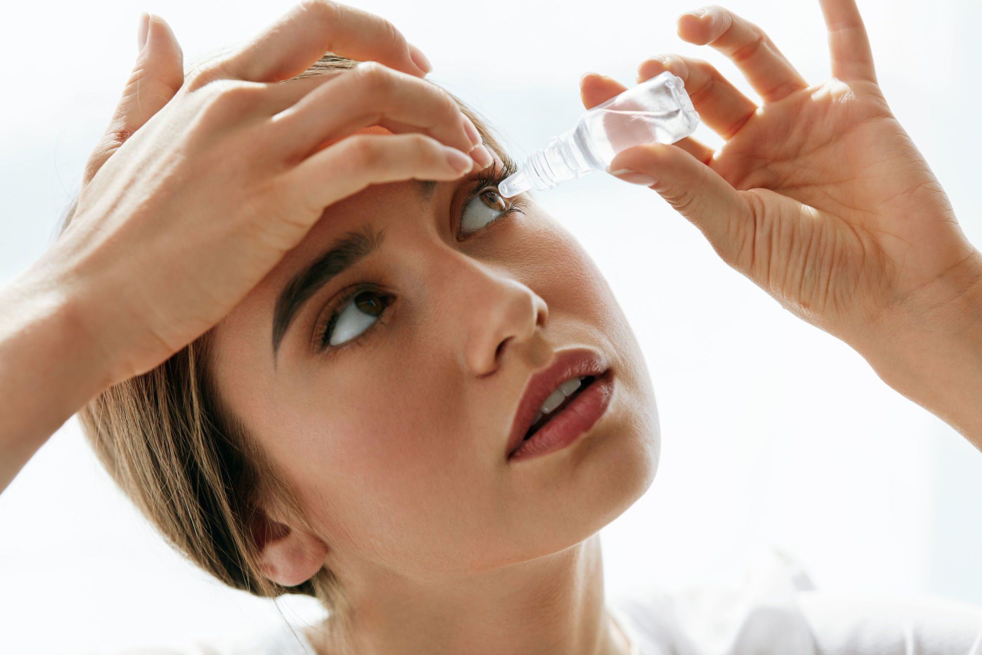 Woman with dry eyes putting lubricating eye drops into her left eye