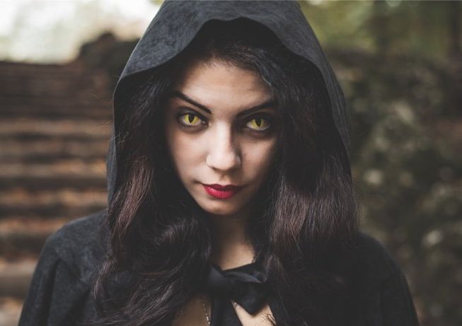 A woman wearing a black cape with a hood and yellow eyes.