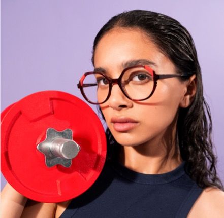 A woman wearing glasses is holding a red dumbbell and wearing woow sunglasses