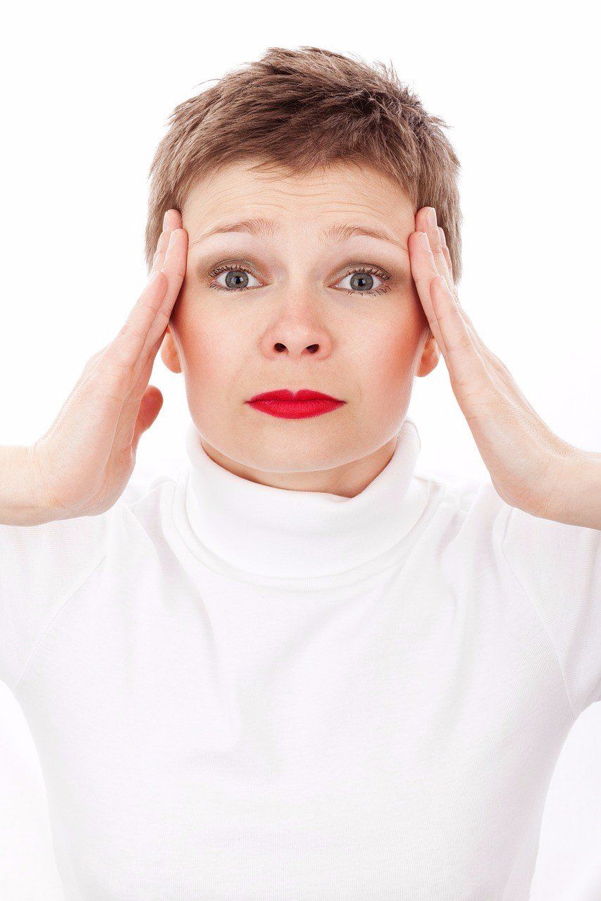 A woman in a white sweater is holding her head with her hands.