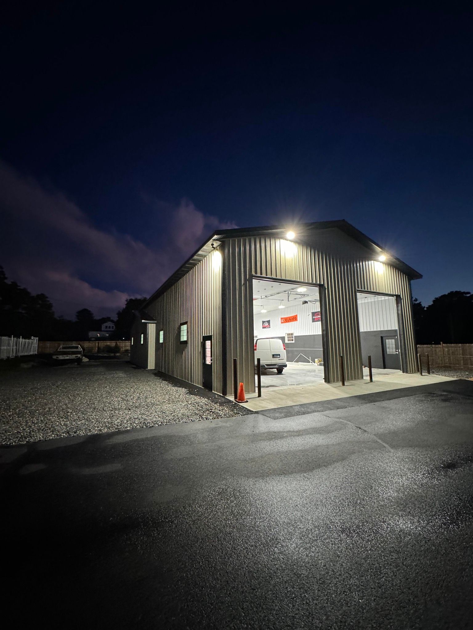 Exterior of a brightly lit industrial building at night, with an open garage door and a vehicle inside.