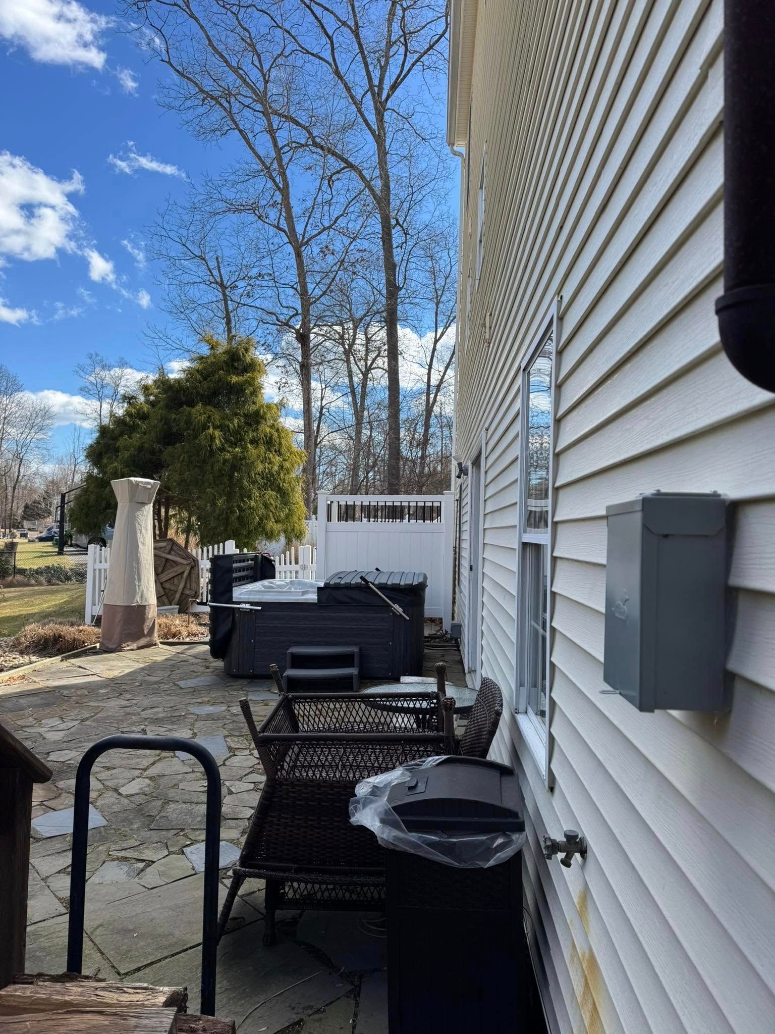 Backyard scene with hot tub, grill, and house with white siding under a blue sky.