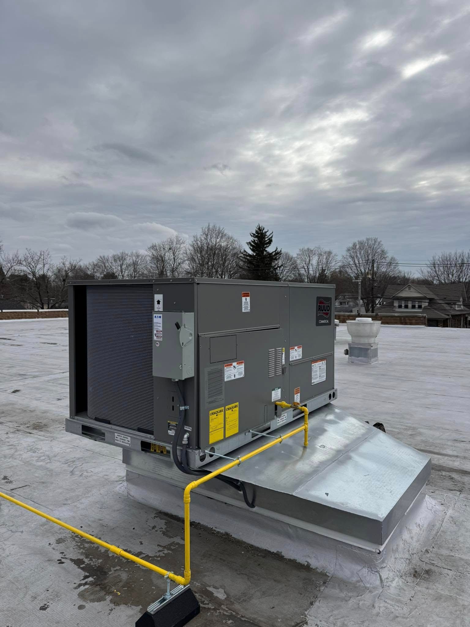 Rooftop HVAC unit on a building with a cloudy sky. Yellow safety rails are installed around the unit.