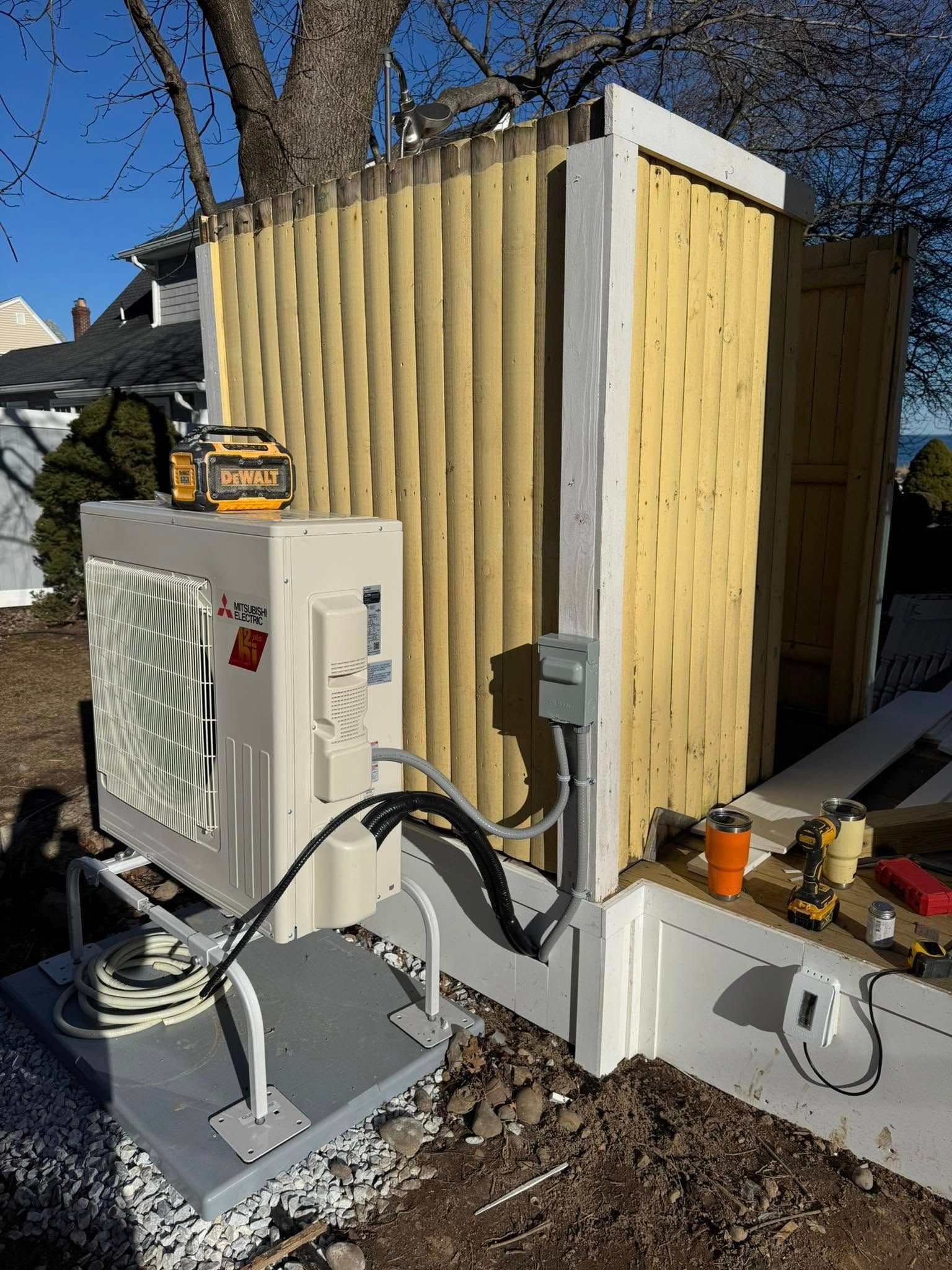 Air conditioning unit installed next to a partially built wooden structure, with electrical conduit and tools visible.