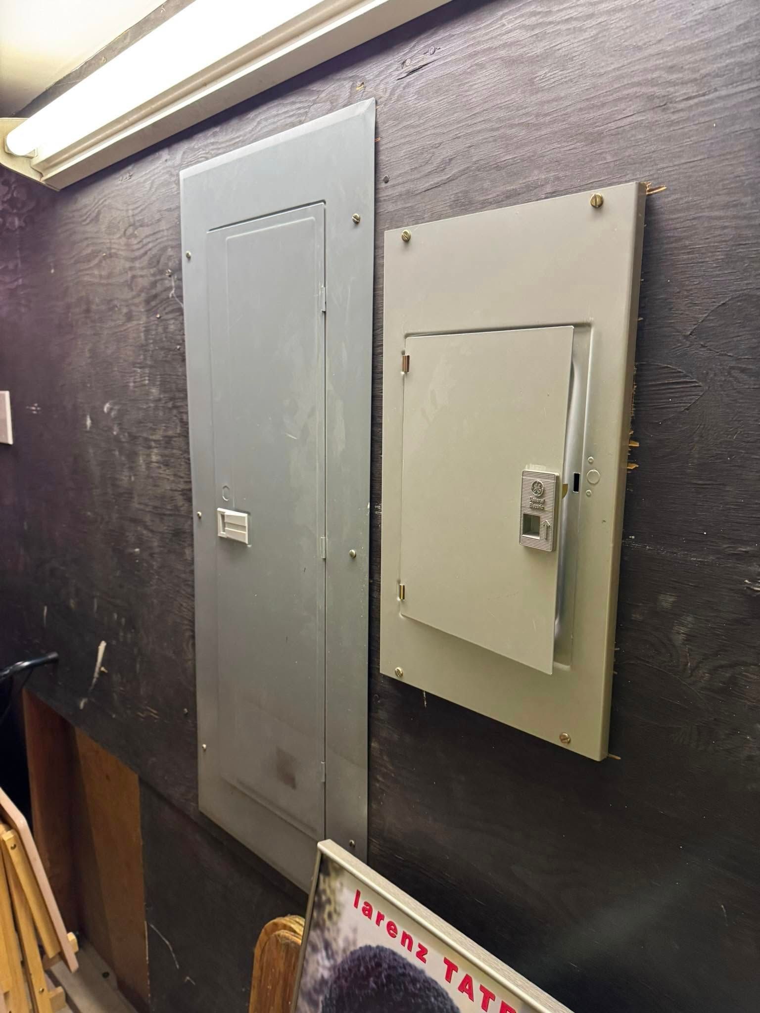Two gray electrical panels mounted on a dark textured wall; record album in the foreground.