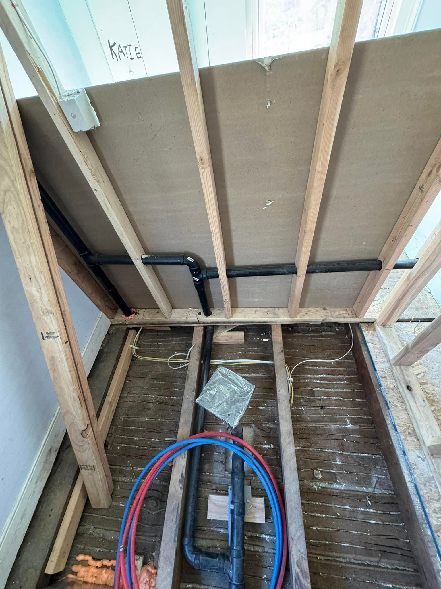 View of construction framing with plumbing pipes and wires.