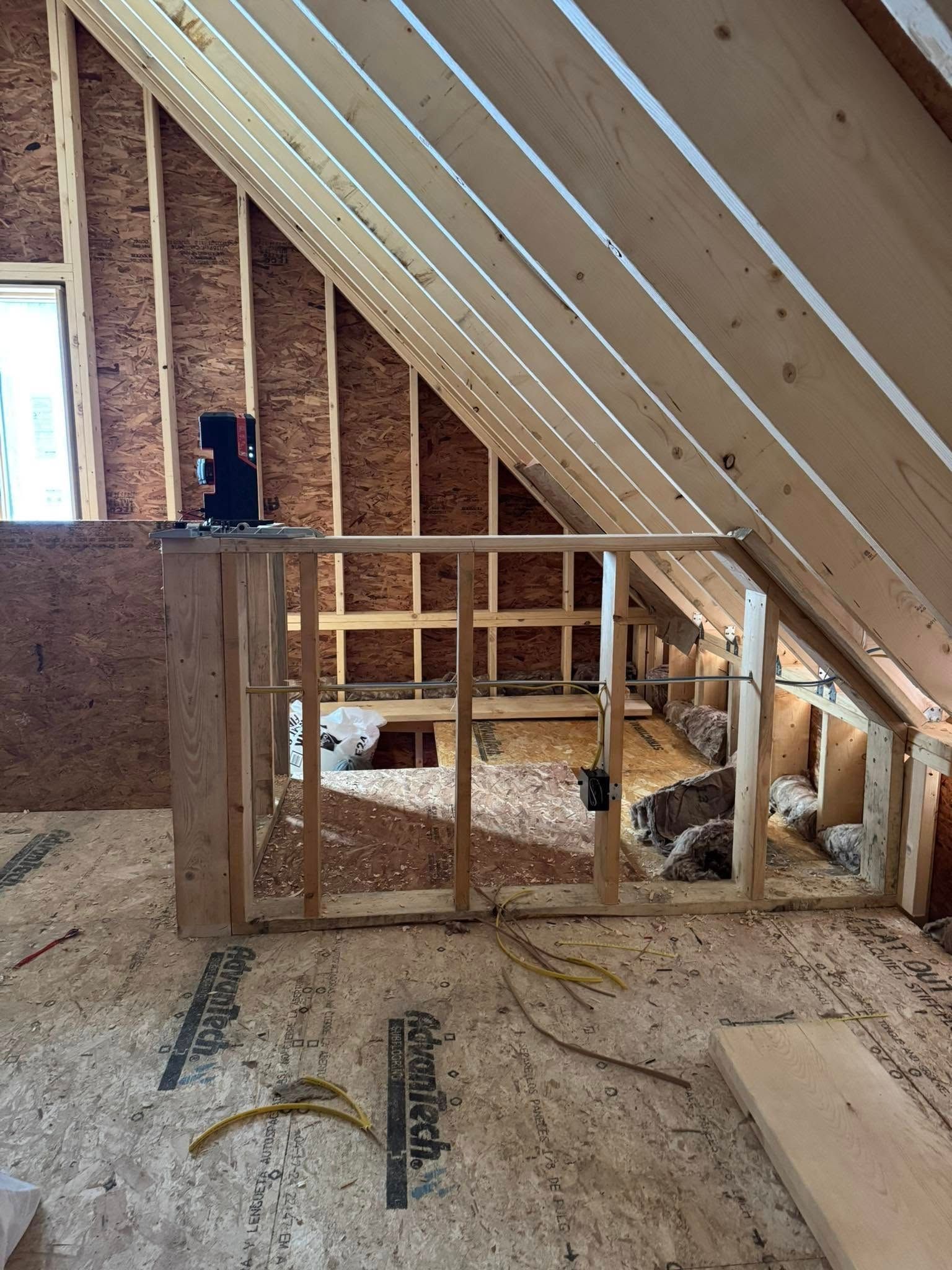 Interior view of an unfinished attic space with wooden framing, exposed insulation, and a partial wall.