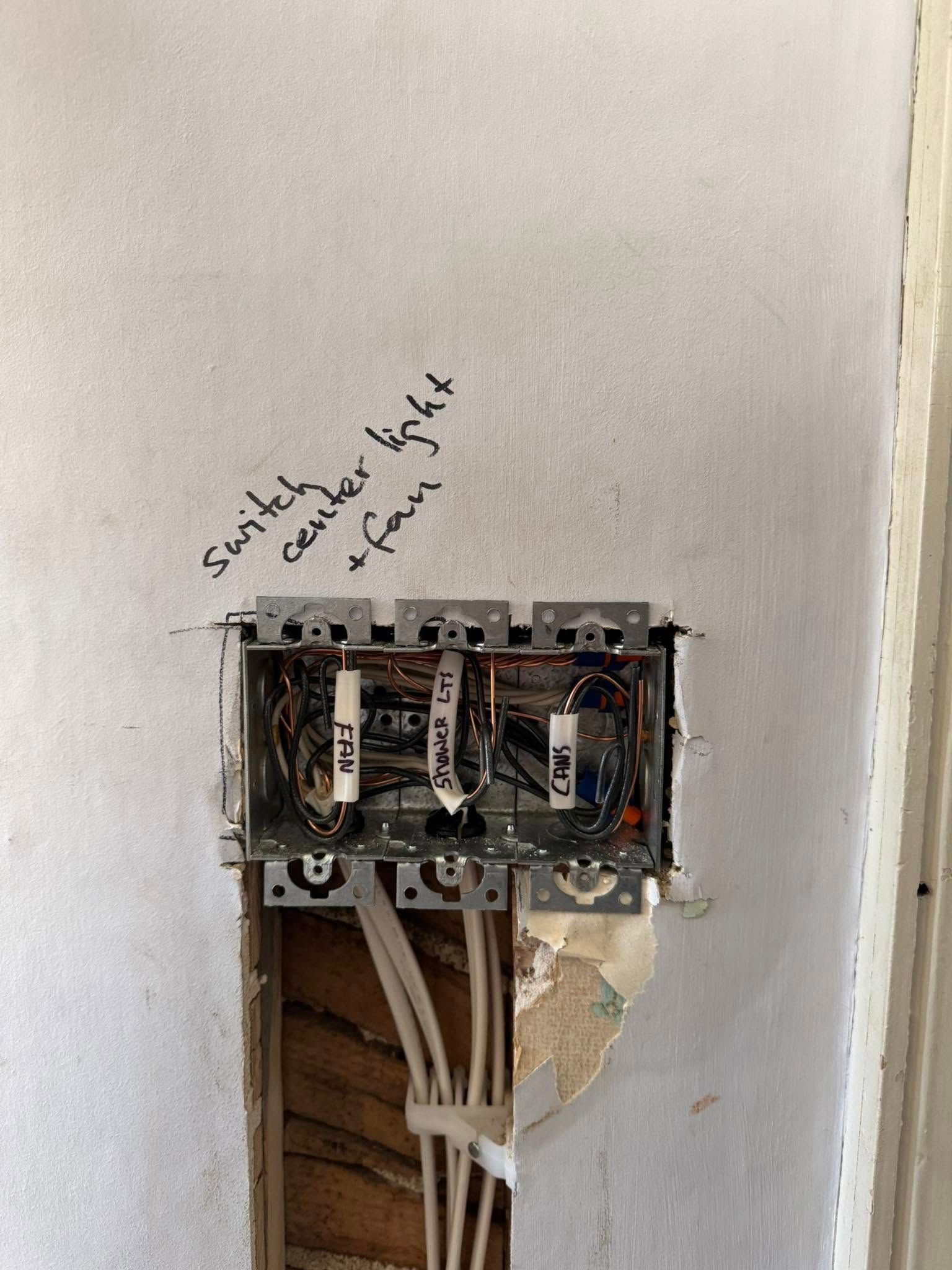Metal electrical box in wall, with wires labeled for switches, ceiling light, and fan.